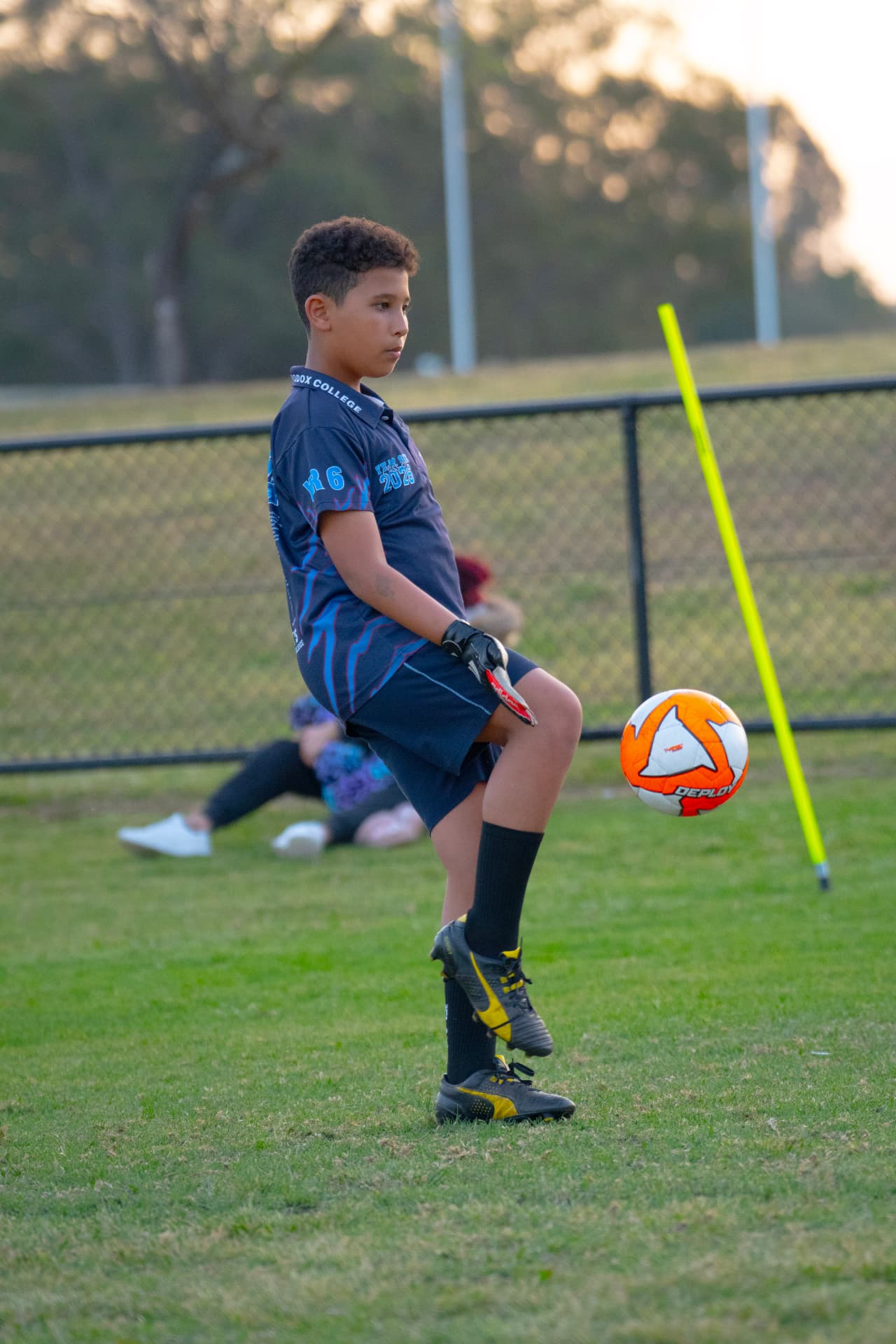 Goalkeeper in a navy kit working the ball at his feet during a handling drill