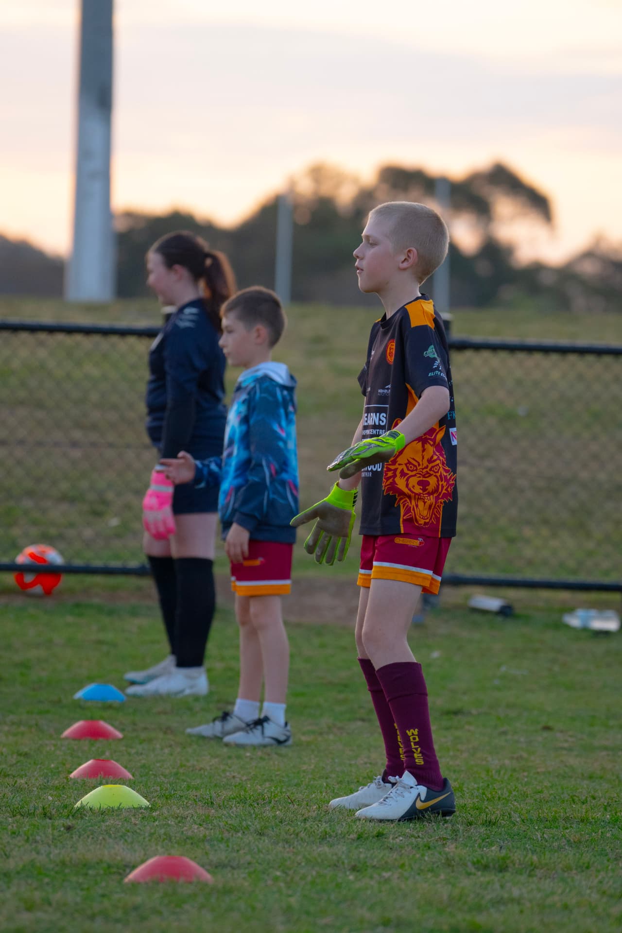 Young goalkeeper in green gloves waiting for the next drill between cones