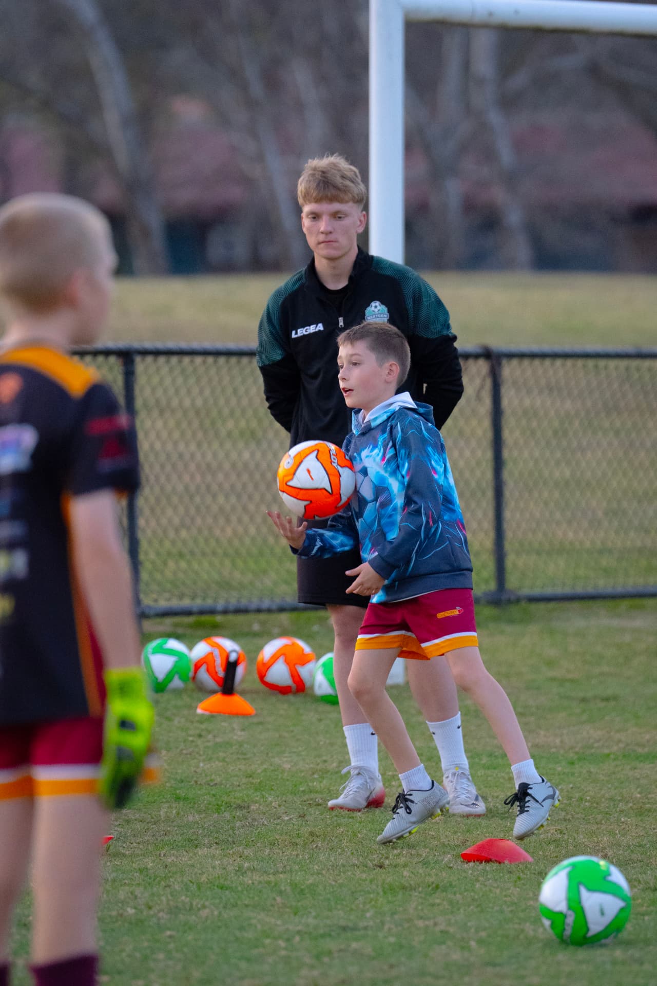 Young player working on ball handling with a coach beside the goal