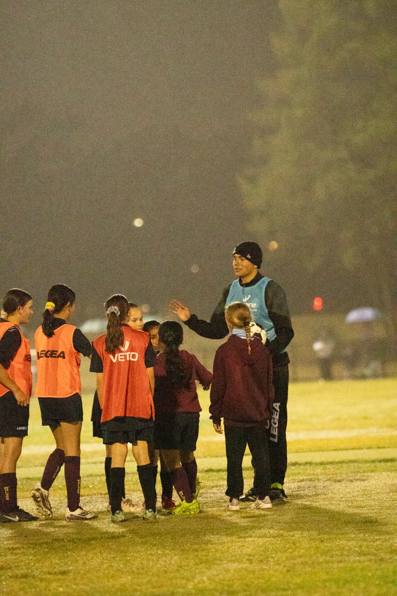 NextGen coach explaining a drill to girls wearing orange bibs
